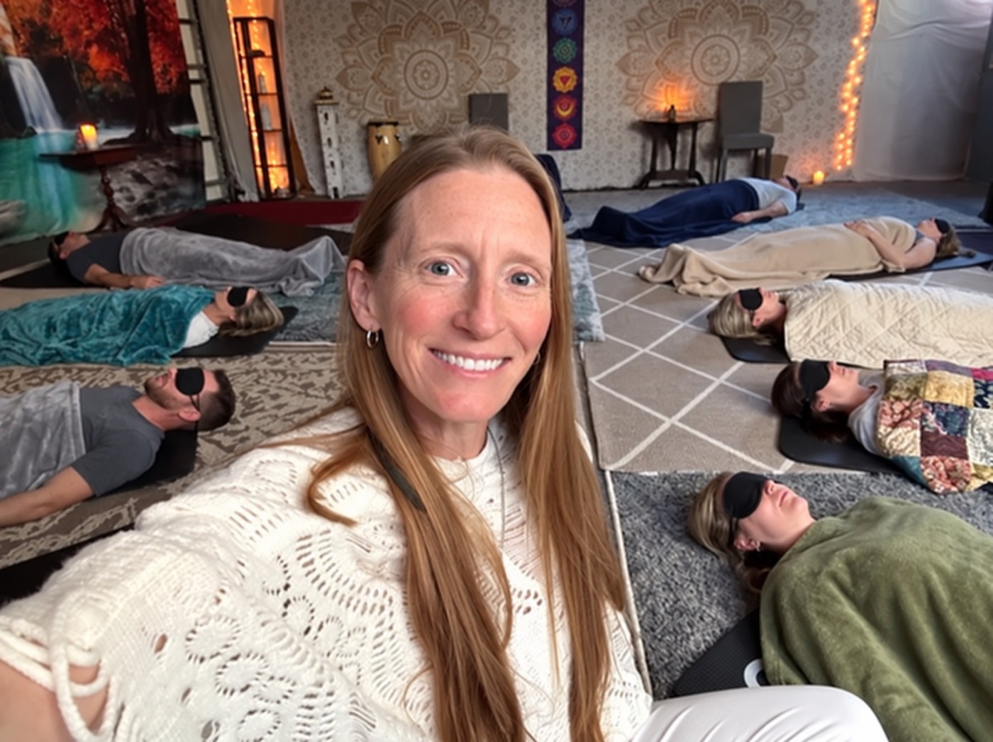 Alissa smiling in the breathwork room while a group rests on mats with eye masks