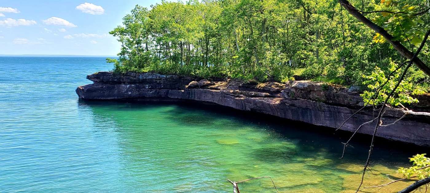 Sandstone ledges topped with trees above clear turquoise Lake Superior water